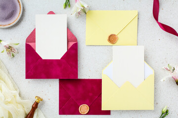 Flat lay composition of magenta and yellow envelopes with blank cards and floral decor.