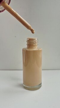 Close-up of liquid foundation dripping from a glass pipette into a bottle.Macro shot of beige makeup concealer or foundation with a dropper on white background.