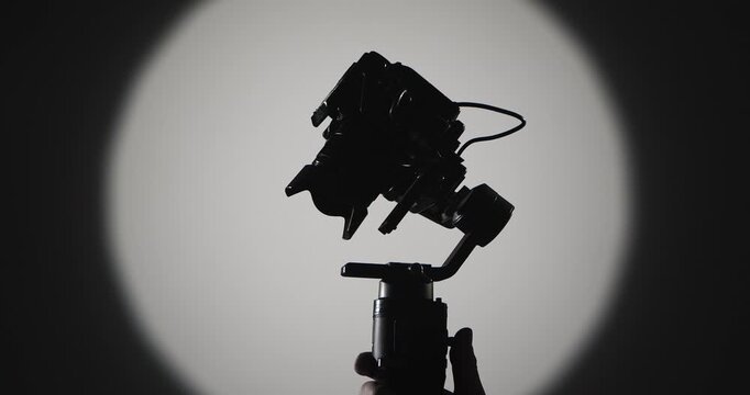 The operator stabilizes the camera mounted on a motorized stabilizer with a suspension, filmed against a bright round light on a dark background, symbolizing film production.