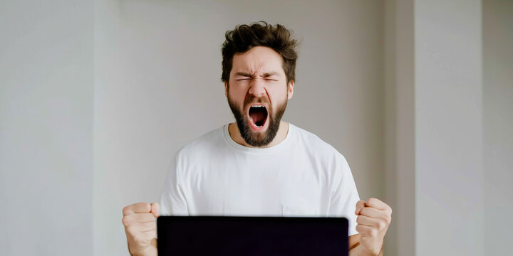Frustrated man yelling with clenched fists at laptop, expressing anger or intense emotion while gaming or working