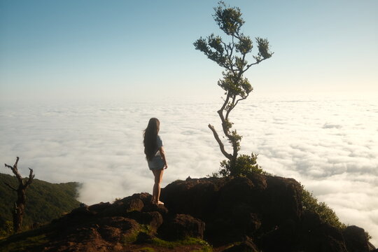 Young Woman Standing Barefoot on Cliff Edge Above the Clouds at Sunrise. Concept of Solo Traveling