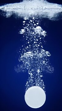 Effervescent tablet dissolving in water with bubbles on blue background