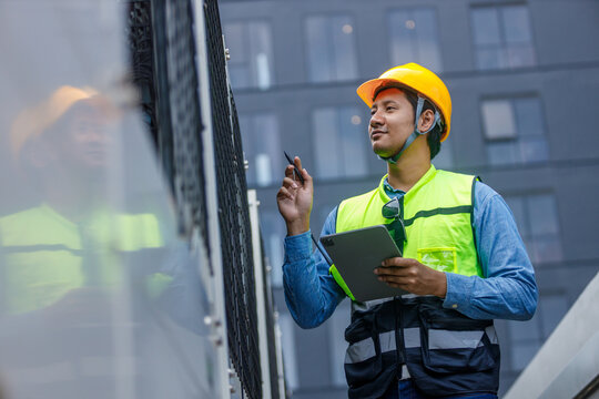 Man engineer using tablet working at rooftop building construction. Male technician worker working checking HVAC of office building. Engineering installing large air conditioning system.