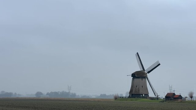 Traditional dutch windmill turning in a misty countryside landscape with blades spinning from wind power on an overcast day