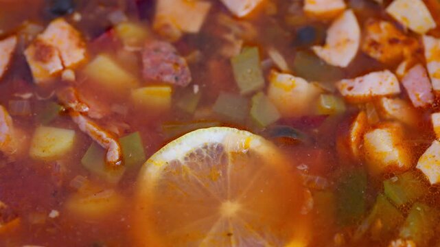 Rich flavorful broth with meats and vegetables, Mouthwatering solyanka with sausage potatoes olives and spices, Warm comforting bowl of smoked meat solyanka with citrus and herbs