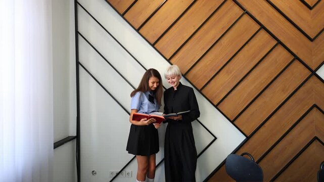 Two students stand side by side in a modern learning space, smiling while reviewing notes together, motivational wall text visible behind them.