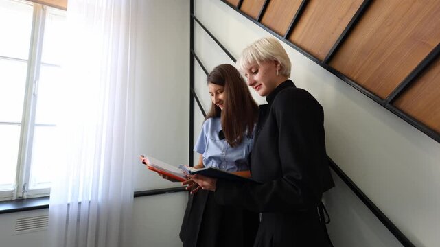 Two students stand side by side in a modern learning space, smiling while reviewing notes together