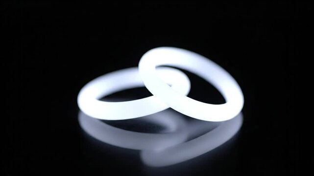 Two illuminated, interlocking rings casting a faint reflection against a stark black background, suggesting connection and unity
