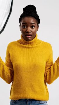 Surprised woman in yellow sweater with raised hands indoors