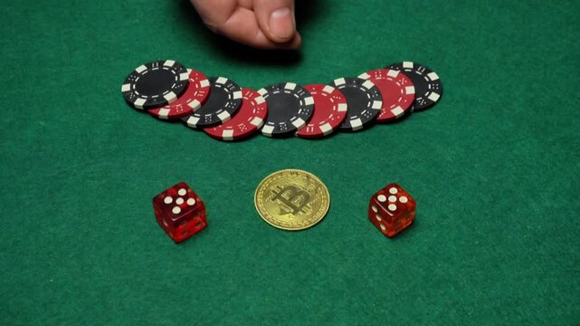 Hand holding a gold coin above a row of poker chips and two red dice on a green felt surface in a gaming setting