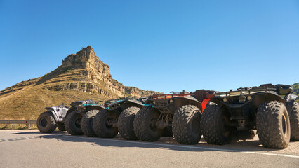 Rental of off-road vehicles for tourist trips. A row of all-terrain vehicles with large wheels in the Alikonovsky Gorge against the backdrop of a blue sky.