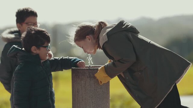 Thirsty children drinking water from a public park fountain