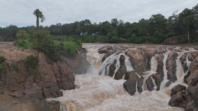 Side view of powerful cascades rushing between rocky cliffs at Khone Phapheng Waterfall.