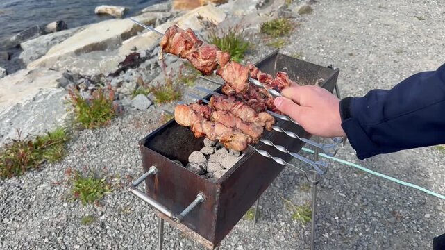 Chef flips meat over glowing charcoal. Urban street food vendor skillfully rotating meat skewers over smoldering charcoal for grilling