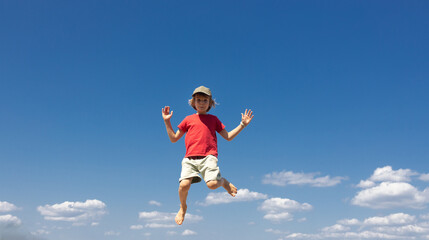 Fototapeta premium barefoot boy joyfully jumps against a blue sky. Concept of freedom and happiness. Energy, active youth, healthy lifestyle, delight, inspiration. Vitality and joy, motivation to move. Space for text.