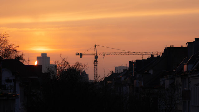 A City under Construction - Sun goes down behind a Building and a big crance is seen - free space