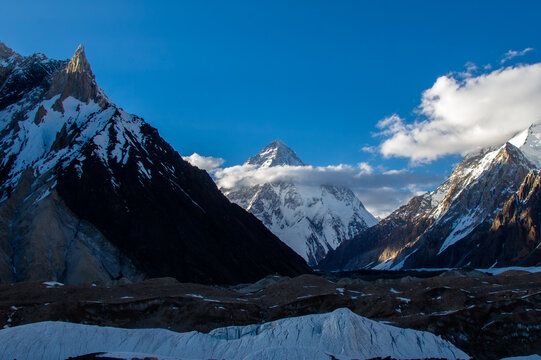 View of snow-capped mountains piercing the sky, their peaks kissed by fluffy clouds, and icy glaciers sprawling below, Skardu, Gilgit, Pakistan.