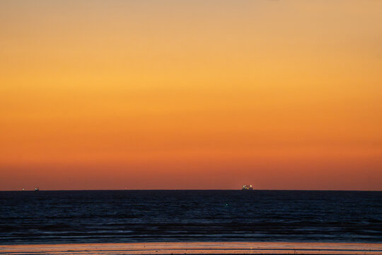 View of the tranquil sea reflects the vibrant sunset sky above, with distant ships adding to the serene horizon, Karachi, Sindh, Pakistan.