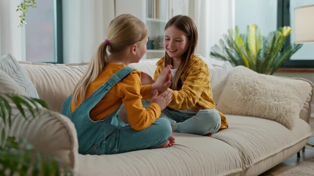 Two little Caucasian girls siblings playing patty cake clapping hands game smiling happy kids sisters friends children daughters play clap palms having fun talking smile talk at home couch family joy
