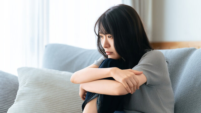 ソファで落ち込んで座る女性の悩みイメージ, Depressed woman sitting alone on a sofa at home