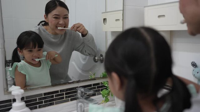 mother teaching girl child to brushing teeth in the bathroom