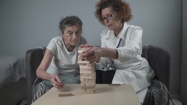 Mature doctor conducting session, therapy for senior patient in nursing home, training fine motor skills for dementia, alzheimer disease and recovery institute by folding wooden blocks, playing.