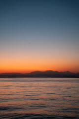 Fototapeta premium Vibrant Orange Sunset over Lake Garda with Mountain Silhouettes and Calm Water