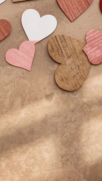 Vertical video: Moving camera revealing pink white woodgrain heart cluster on kraft mat, copy space