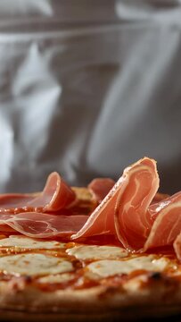 Vertical video: Reaching chef placing prosciutto on mozzarella pizza at prep in white coat to serve