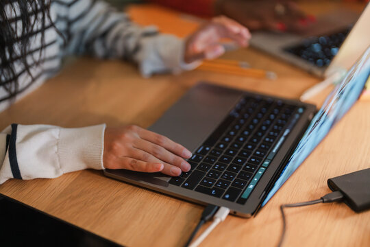 A person's hands are shown typing on a laptop keyboard, with cables connected to the device and a portable power bank.