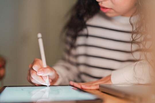A person uses a stylus to draw on a digital tablet in a dimly lit room, focusing on their creative work.