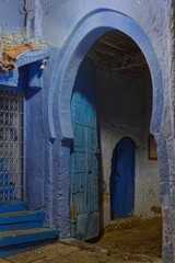 Naklejka premium Gateway of a traditional house in the medina at night, with the customary blue paint on its chipped walls and thick wood door. Chefchaouen-Morocco-018