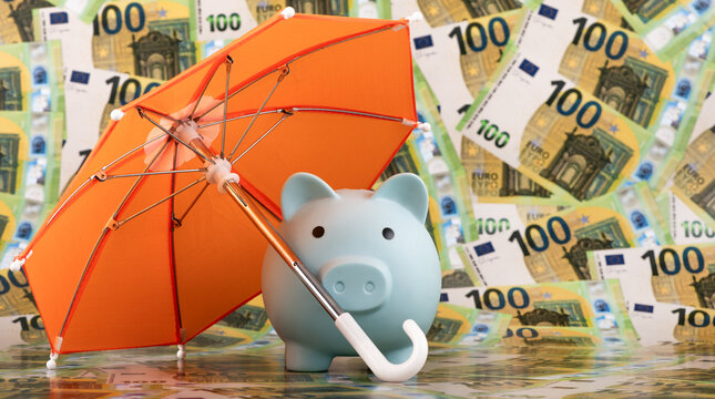 A blue piggy bank protected by an umbrella against a background of 100 euro bills