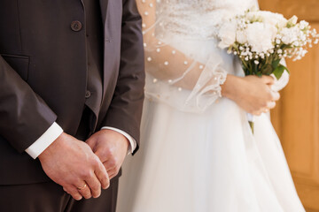 Close-up of bride and groom holding hands at wedding ceremony with white bouquet and elegant attire