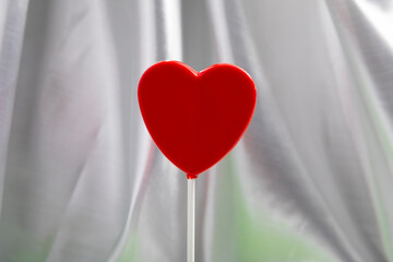 Minimalist composition featuring two red heart-shaped lollipops on a soft fabric background. The clean design and balanced symmetry make this image ideal for graphic design projects, website headers, 