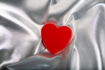 A mininalist red chocolate candy heart resting on soft, flowing silver fabric, symbolizing love, romance, and sweet indulgence. The elegant contrast and minimal composition make this image ideal for V