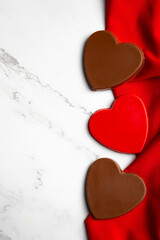 Heart-shaped chocolate candies arranged on rich red fabric over a white marble background with ample copy space. This clean and elegant composition is ideal for Valentine&rsquo;s Day promotions
