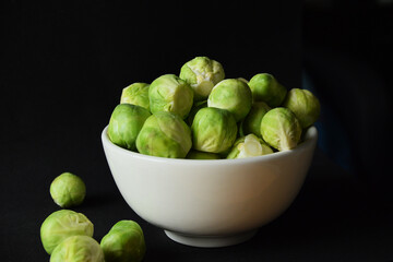 Fresh raw Brussels sprouts in white bowl on black background