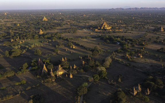 Aerial view of pagodas and temples scattered across the arid landscape, casting long shadows in the golden light of dawn, Old Bagan, Mandalay Region, Myanmar.
