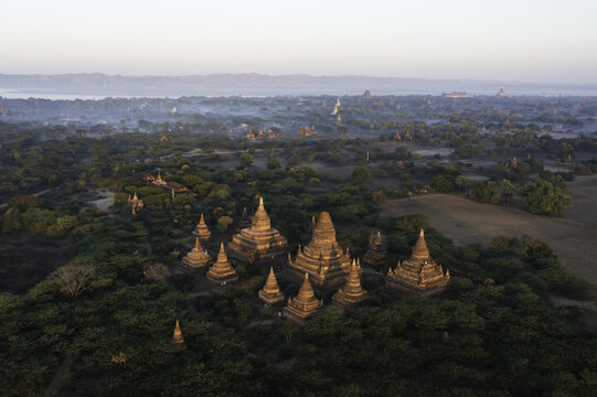 Aerial view of ancient temples and pagodas piercing through the lush green canopy in the misty morning light, Old Bagan, Mandalay Region, Myanmar.