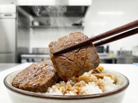 Closeup of Chopsticks Lifting Tender Beef Slice Over Rice Bowl