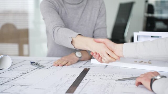 Handshaking between two architects finalizing a construction project deal, business partners agreeing on engineering blueprints and architectural models in an office, close up