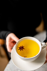 Hand holding cup of golden milk/turmeric latte with star anise spice