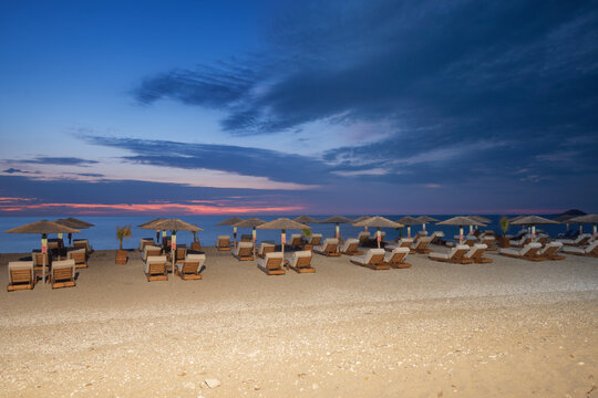 View of beach chairs and umbrellas line the sandy shore as the sky transitions from dusk to night in Kathisma Beach, Kathisma, Lefkada, Greece.