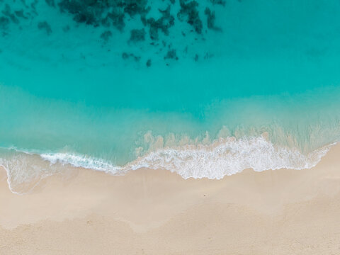 Aerial view of turquoise waters meeting the pale sands of a pristine beach, where gentle waves create a frothy white line, Anse Reunion, La Digue, Seychelles.
