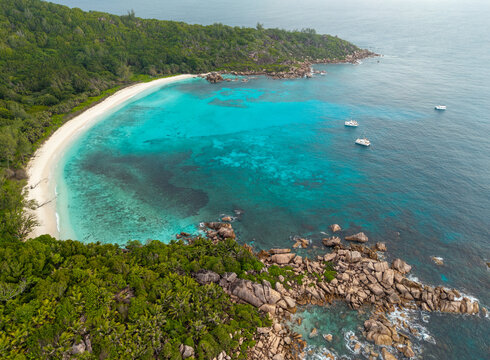 Aerial view of the beach with turquoise waters meeting the verdant coastline, where boats float gently, Anse Reunion, La Digue, Seychelles.