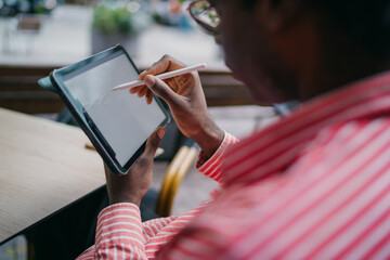 African freelancer drawing on tablet with stylus in relaxed urban setting, reflecting freedom, concentration and digital creativity in flexible modern workspace. © BullRun
