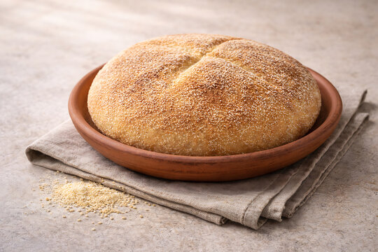 Moroccan khobz semolina bread  round rustic loaf  clay plate  natural daylight