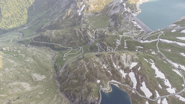 Aerial view of serpentine roads winding through the rugged terrain near Lago Serru and Lago Agnel, kissed by lingering snow patches, Colle del Nivolet, Valle d'Aosta, Italy.