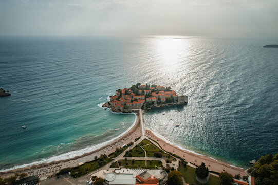 Aerial view of Sveti Stefan island, a jewel of terracotta roofs amidst azure waters, linked by a slender isthmus of golden sand, Sveti Stefan, Budva Municipality, Montenegro.